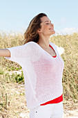 A woman with long hair wearing a red top and white summer jumper