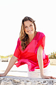 A woman with long hair wearing a red and pink tunic and white shorts