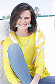 Junge Frau in gelbem Langarmshirt mit Pulli über den Schultern und Jeans