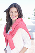 A young woman wearing a white summer jumper and a fuchsia-coloured jumper over her shoulders