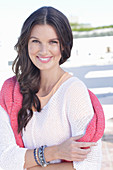 A young woman wearing a white summer jumper and a fuchsia-coloured jumper over her shoulders