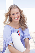 A young blonde woman wearing a blue-and-white striped Carmen blouse and white trousers