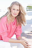 A young blonde woman wearing a pink blouse with gigot sleeves and white trousers