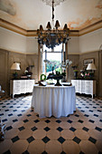 Antique chests of drawers, round table and chandelier in stylish foyer