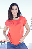 A mature brunette woman wearing a red blouse and jeans