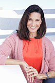 A mature brunette woman wearing a red blouse and a wrap-around jumper