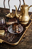 Golden jug, cup and metal candle holder on tray