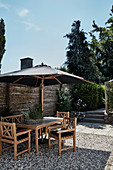 Shallow wicker basket planted with herbs in seating area with parasol on gravel terrace