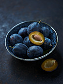 Fresh plums in a bowl on a dark surface