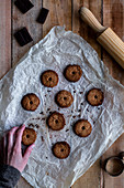 Hands holding chocolate baked cookies on white baking paper with chocolate