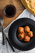 Cooked meatballs with tomato sauce serving with bread on black plate with cutlery and beverage