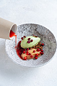 Bowl with slice of red fish and avocado served with red berries and pouring with red sauce