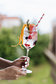 Female carrying cold drink with berries and grapefruit decorated with rosemary twig and orange peel