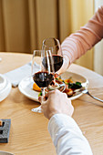 Couple clinking glasses of red wine and proposing toast during lunch in luxury restaurant