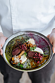 Person holding plate, rare steak with cranberry sauce served with herbs, mushrooms and cheese