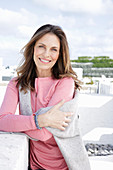 A long-haired woman wearing a pink top with a grey jumper over her shoulders