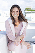 A long-haired woman wearing an apricot top and a pink jumper with a white jumper over her shoulders