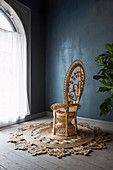 Peacock chair on sisal rug against dark blue wall and next to large arched window