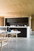 Dining table and designer chairs in front of open-plan kitchen in architect-designed house