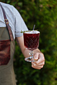Person holding fresh tasty red cocktail with straw in glass in green garden