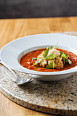 Appetizing fresh tomato soup with greens on white plate on marble stand