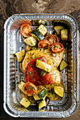 Slice red tomatoes, zucchini sprinkled with herbs and sauces in shiny baking form
