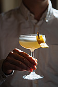 Cropped person holding fresh appetizing cocktail in glass festively decorated with clothespin