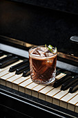 Glass of cocktail with ice resting on a piano keys