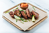 Grilled chicken wings on wooden board with slices of lime herbs and red sauce