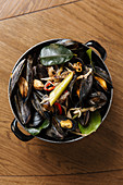 Black mollusk dish with assorted steamed vegetables in black pot on table