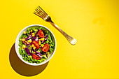 Veganer Salat mit Kirschtomaten, roten Zwiebeln und Mais auf gelbem Untergrund