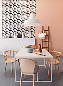 Pastel-pink wall, wallpaper with graphic pattern and tiled dado in dining room