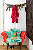 Antique armchair with brightly coloured upholstery next to African, carved, wooden doors decorating wall