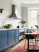 Blue cupboards in cosy kitchen-dining room with dining table on kilim rug