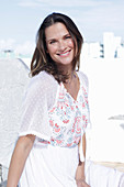 A long-haired woman wearing a white summer dress with colourful embroidery detail