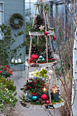 Self-made hanging étagère with wooden discs, cones, pine branches, balls, Christmas rose, false berries and lanterns as decoration