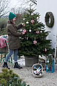 Woman decorates Nordmann fir with stars and balls