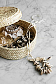 Jewellery made from shells in raffia basket on marble tile