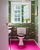 Pinker Boden im kleinen Bad mit Toilette und grüner Tapete
