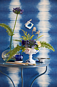 Gesteck mit Schmucklilie und Farn vor Wand mit Ikat-Muster in Blau