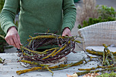 Schneeglöckchen in Kranz aus Zweigen : Frau windet Kranz aus flechtenbewachsenen Zweigen, Birke und Weide