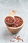 Red rice in a wooden bowl and a wooden scoop