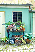 Pflanzen und Vintage-Deko auf und vor einem Tisch vor grünem Haus