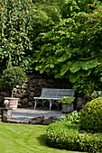 Bank vor rustikaler Steinmauer im üppig grünen, gepflegten Garten