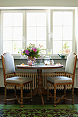 Two upholstered chairs with turned legs at pedestal table below window