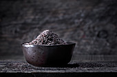 Poppyseeds in a black bowl against a black background