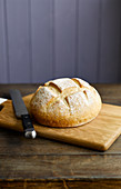 A round loaf of white bread on a chopping board with a knife