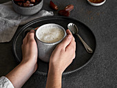 Hands holding a cup of date and soy drink