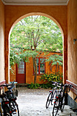 Bicycles in arched passageway leading into summery courtyard