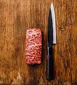 Marmoriertes rohes Steak vom Wagyu-Rind mit Messer auf Holzuntergrund